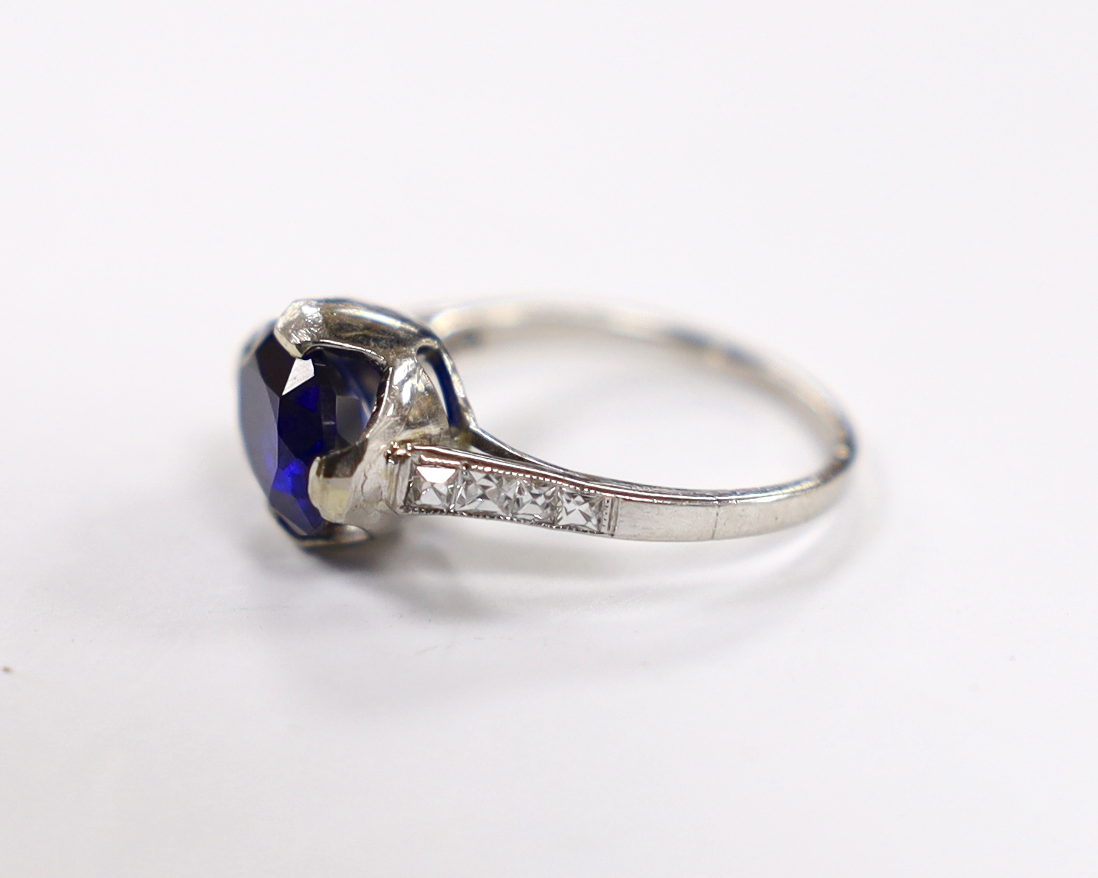 A plat. and iridium, single stone oval cut synthetic sapphire set ring, with graduated diamond chip set shoulders, the shank bearing the signature 'Tiffany & Co', size G, gross weight 3.7 grams.